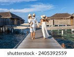 A beautiful family walks over a wooden pier between water lodges in the Maldives islands during their vacations