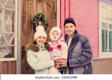 Beautiful Family In Warm Clothes Standing  Of His House In Winter