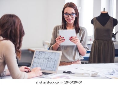 Beautiful fashion designers are using gadgets and smiling while working in office - Powered by Shutterstock