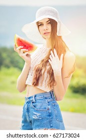 Beautiful fashion girl in summer, outdoors on sunny day, holding slice of watermelon, wearing denim shorts, crochet crop top and floppy hat. Modern woman posing with fresh fruit. Retouched.