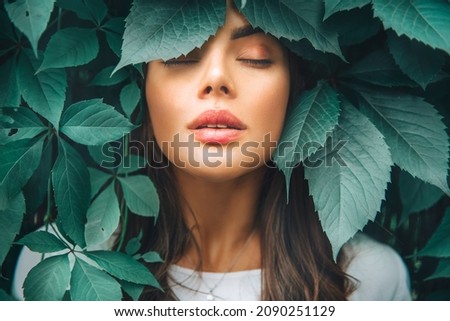 Beautiful fashion model girl enjoying nature, breathing fresh air in summer garden over Green leaves background. Harmony concept. Healthy beauty woman outdoor portrait. Zen. 
