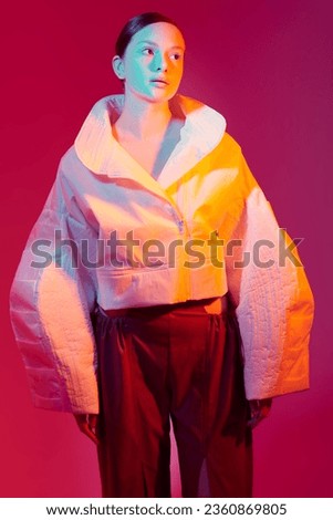 Beautiful fashion model girl posing in stylish clothes with wide oversized shapes. Studio shot against a red background in mixed color light. Bright colors. Fashion and haute couture style. 
