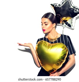 Beautiful fashion model party girl with colorful heart and star shaped balloons posing at studio isolated on white. Beauty sexy woman celebrating, showing empty copy space on open hand palm for text