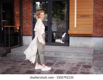 Beautiful Fashion Model Smiling On City Street. Stylish Woman Wearing Fashionable Spring Or Autumn Clothes (beige Trench Coat, Oversize Khaki Cargo Pants, Accessorie) Outdoors. Trend Outfit