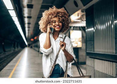 Beautiful fashionable black woman standing at a subway train station. She is happy and talking to someone on her smart phone. Public transportation and urban life concept. - Powered by Shutterstock