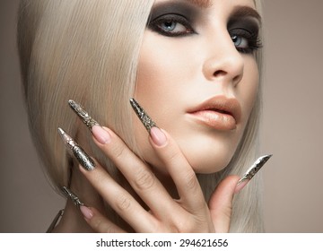 Beautiful fashionable girl in a glamorous image with bright makeup and long silver nails. Art design manicure. Picture taken in the studio.