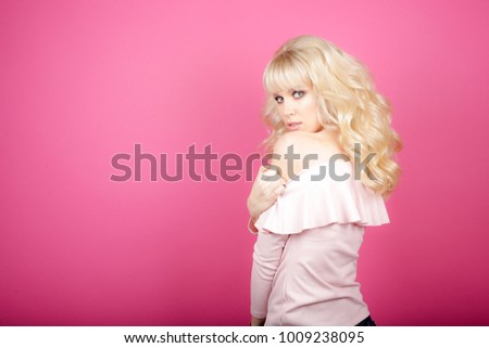 Beautiful fashionable girl haired with long curly hair in a pink blouse. The girl in the studio on a pink background.Advertising, hair products, beauty salon, cosmetics, clothing.