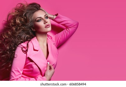 Beautiful fashionable girl with long curly hair in a pink jacket. Girl in the studio on a pink background.Advertising, hair products, beauty salon, cosmetics, clothing. Fashion, boutique. Pink.