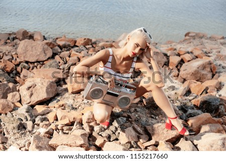 beautiful fashionable girl posing with retro boombox on rocky beach