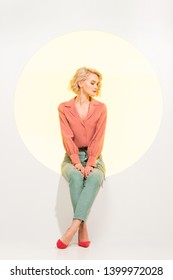 beautiful fashionable girl posing while sitting on yellow circle with white background
