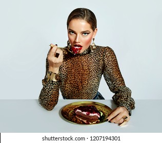 A beautiful, fashionable, luxurious girl with bright makeup and in a leopard blouse is eating a cherry cake with a golden fork from a golden plate.fashion, beauty, makeup, cosmetics, beauty salon.