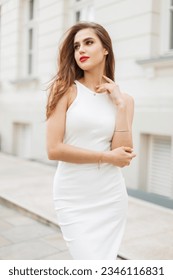 Beautiful fashionable vogue girl model with an elegant white dress walks in the city near a vintage white building. Pretty lady