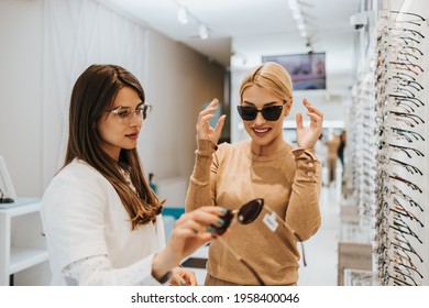 Beautiful and fashionable woman choosing eyeglasses frame in modern optical store. Female seller specialist helps her to make right decision. - Powered by Shutterstock