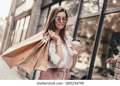 Beautiful fashionable woman drink coffee walking near mall with shopping bags.