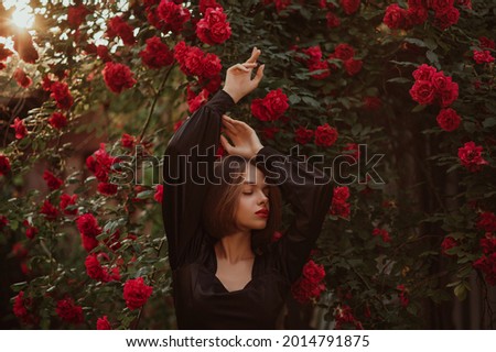 Beautiful fashionable woman with red lips makeup posing outdoor, in blooming rose garden. Copy, empty space for text