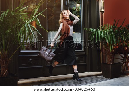 Beautiful fashionable young woman running with bag. City lifestyle. Female fashion. Full body portrait.