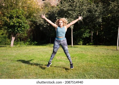 beautiful fat blonde woman playing sports in the park. She is jumping on the grass, spreading her arms and legs. Outdoor sport and calisthenics concept. Healthy life.