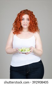 beautiful fat girl with red hair with a plate of salad in hand on gray background
