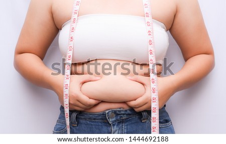 A beautiful fat woman with a tape measure. She uses her hand to squeeze the excess fat that is isolated on a white background. She wants to lose weight, the concept of surgery and break down fat under