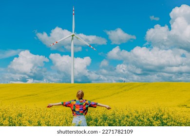 Beautiful female in 90s stylish shirt in rapeseed field with wind turbine on background - Powered by Shutterstock