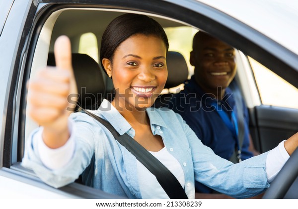 beautiful female african learner driver with\
instructor giving thumb\
up