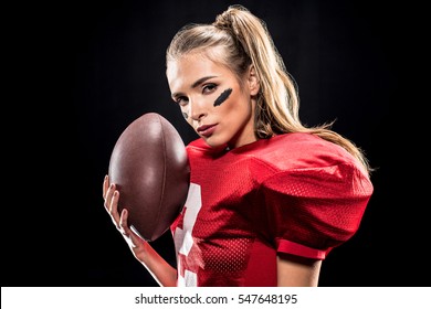 Beautiful female american football player with ball looking at camera isolated on black
