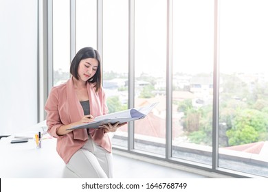 
Beautiful Female Asian Worker Holding A Folder File Of Documents And Information On Work Or Business Looking, Reading, Learning From The Documents, While Holding A Pen Working In Office Environment