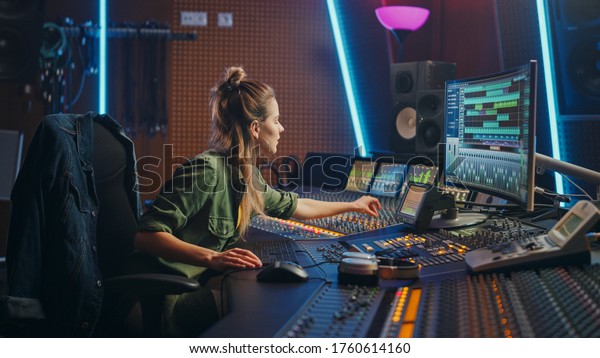 Beautiful Female Audio Engineer Working in Music\
Recording Studio, Uses Mixing Board and Software to Create Modern\
Sound. Creative Girl Artist Musician Working on Control Desk to\
Produce New Song
