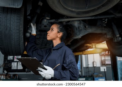 Beautiful female auto mechanic checking wheel tires in garage, car service technician woman repairing customer car at automobile service, inspecting vehicle underbody and suspension engine system. - Powered by Shutterstock