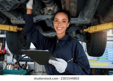 Beautiful female auto mechanic checking wheel tires in garage, car service technician woman repairing customer car at automobile service, inspecting vehicle underbody and suspension engine system. - Powered by Shutterstock