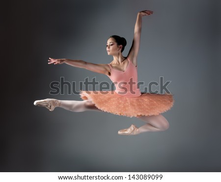 Beautiful female ballet dancer on a grey background. Ballerina is wearing an orange tutu, pink stockings and pointe shoes.