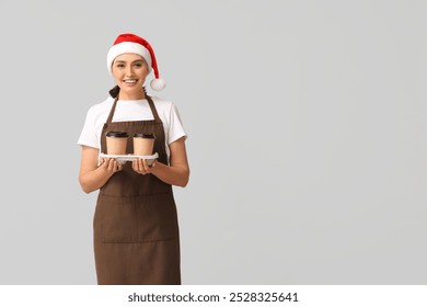 Beautiful female barista in Santa hat with cups of coffee on grey background - Powered by Shutterstock