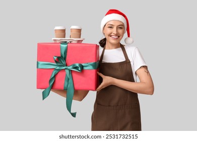 Beautiful female barista in Santa hat with cups of coffee and gift box on grey background - Powered by Shutterstock