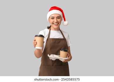 Beautiful female barista in Santa hat with cups of coffee on grey background - Powered by Shutterstock