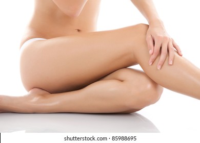 Beautiful Female Body Isolated Over White Background. Sitting On The Floor Touch Leg By Hand, Beauty And Skin Care Concept.