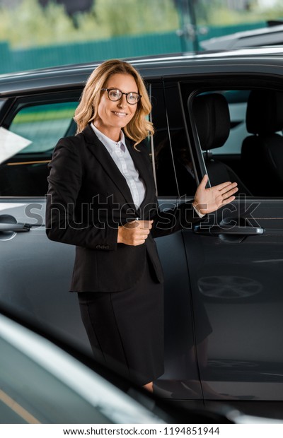 beautiful\
female car dealer pointing at car in\
showroom