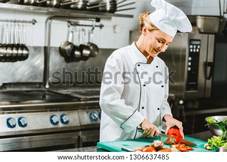beautiful female chef in uniform cutting pepper in restaurant kitchen