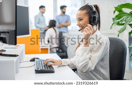 Beautiful female consultant of call center in headphones working on computer at office.