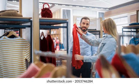 Beautiful Female Customer Shopping In Clothing Store, Retail Sales Associate Helps With Advice. Diverse People In Fashionable Shop, Choosing Stylish Clothes, Colorful Brand With Sustainable Designs