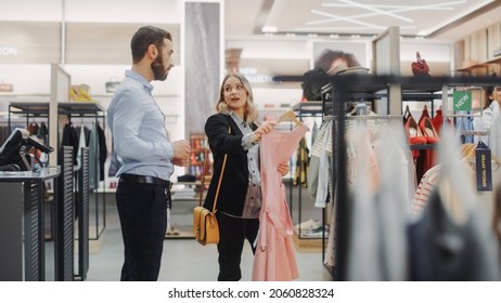 Beautiful Female Customer Shopping In Clothing Store, Retail Sales Associate Helps With Advice. Diverse People In Fashionable Shop, Choosing Stylish Clothes, Colorful Brand With Sustainable Designs