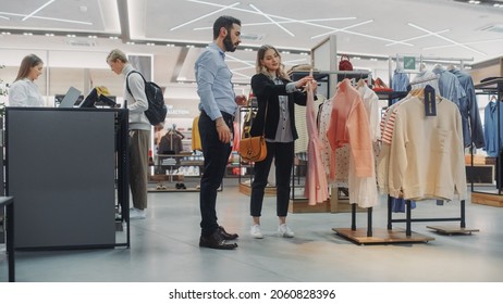 Beautiful Female Customer Shopping In Clothing Store, Retail Sales Associate Helps With Advice. Diverse People In Fashionable Shop, Choosing Stylish Clothes, Colorful Brand With Sustainable Designs