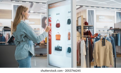 Beautiful Female Customer Using Floor-Standing LCD Touch Display while Shopping in Clothing Store. She is Choosing Stylish Bags, Picking Different Designs from Collection. People in Fashionable Shop. - Shutterstock ID 2053746245