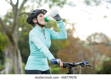 Beautiful female cyclist drinking water in forest