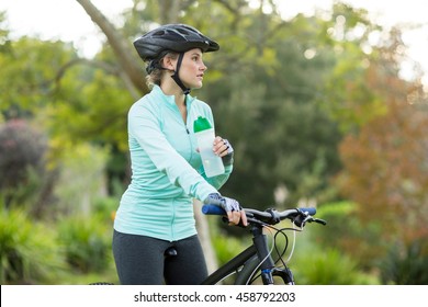 Beautiful female cyclist drinking water in forest at countryside - Powered by Shutterstock