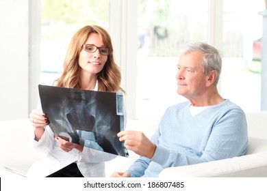 Beautiful female doctor analyzing x-ray with senior patient at small clinic. - Powered by Shutterstock