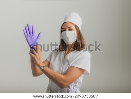A beautiful female doctor or nurse in a protective mask and rubber gloves on a light background with copyspace. Healthcare concept