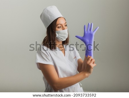 A beautiful female doctor or nurse in a protective mask and rubber gloves on a light background with copyspace. Healthcare concept