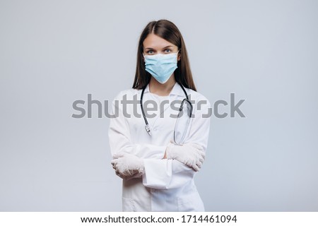 Beautiful female doctor or nurse wearing protective mask and latex or rubber gloves on grey background with copyspace. Health care concept
