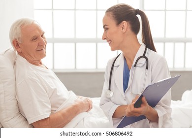 Beautiful Female Doctor In White Medical Coat Is Talking With Her Old Patient And Smiling