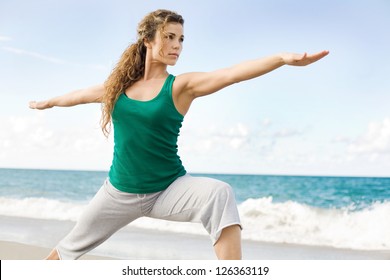 Beautiful female doing yoga warrior pose at the beach with copy space